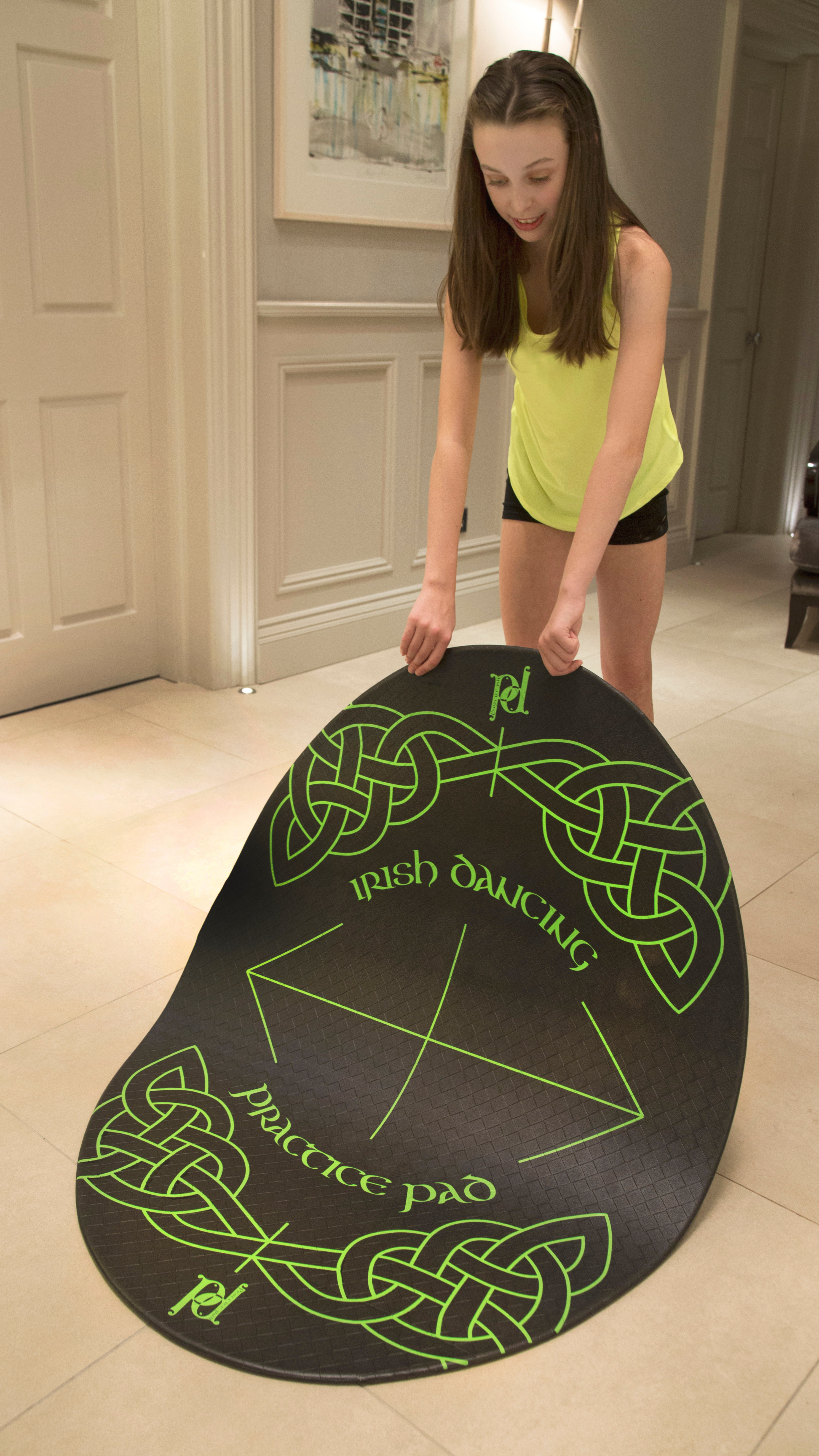 Person holding a large black and green Irish dance practice pad in a room.
